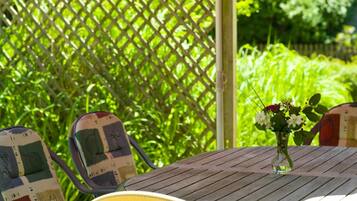An outdoor patio with a wooden table, a yellow chair, and a red umbrella.