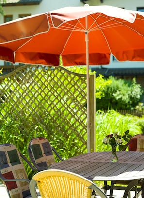 An outdoor patio with a wooden table, a yellow chair, and a red umbrella. - Vitalhotel Garni Vier Jahreszeiten (Bad Fuessing)