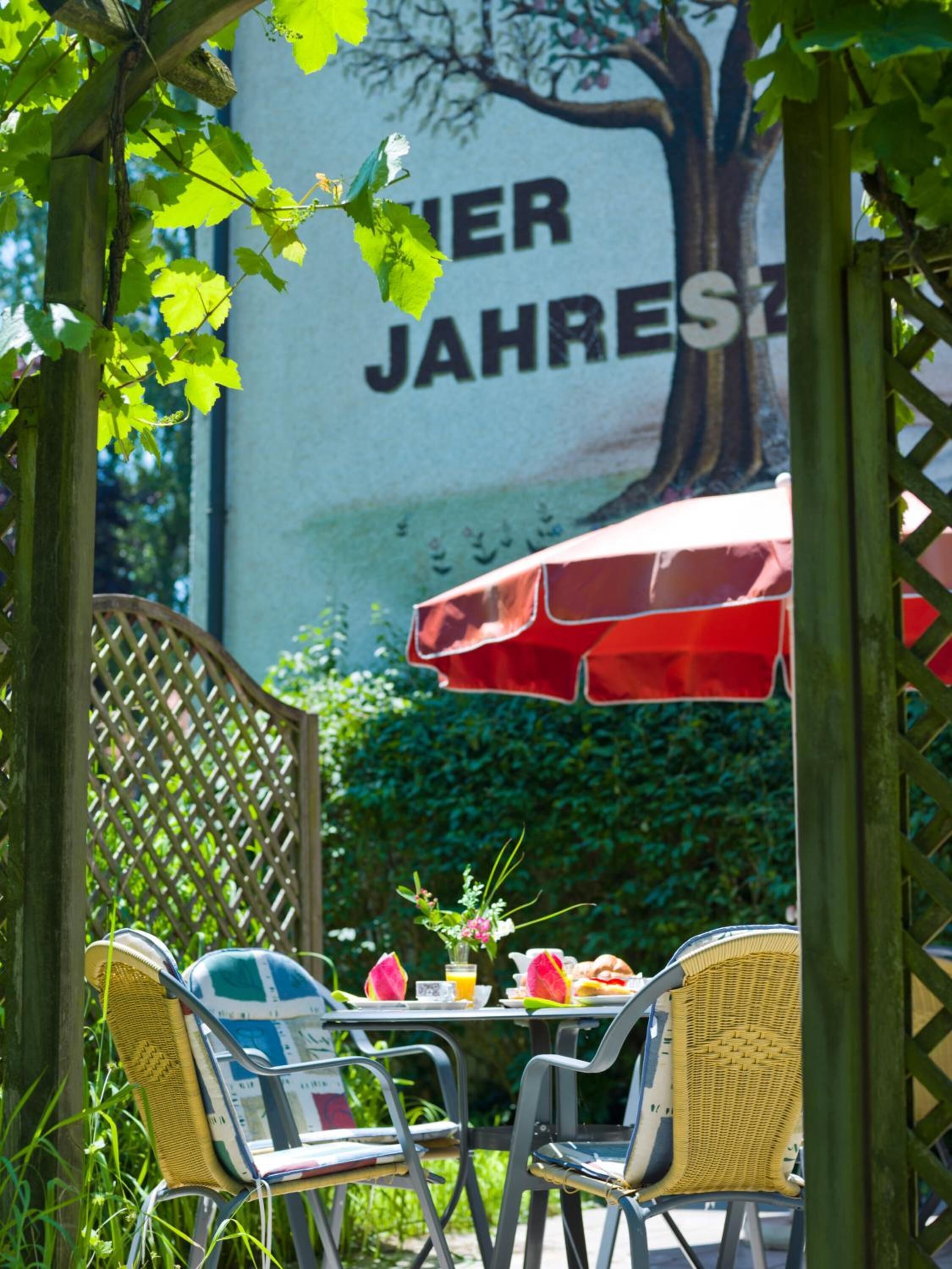 An outdoor seating area with wicker chairs and a table set for two, under a red umbrella.