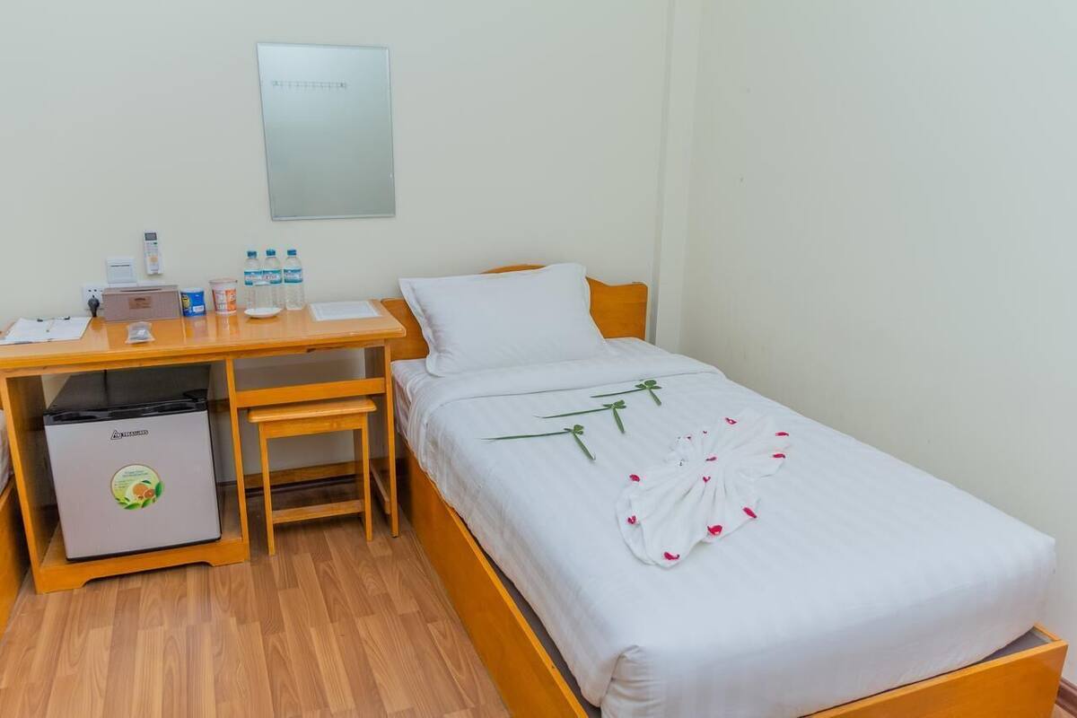 Une chambre d’hôtel équipée d’un lit, d’un bureau, d’une chaise, d’une petite poubelle et d’un miroir fixé au mur.