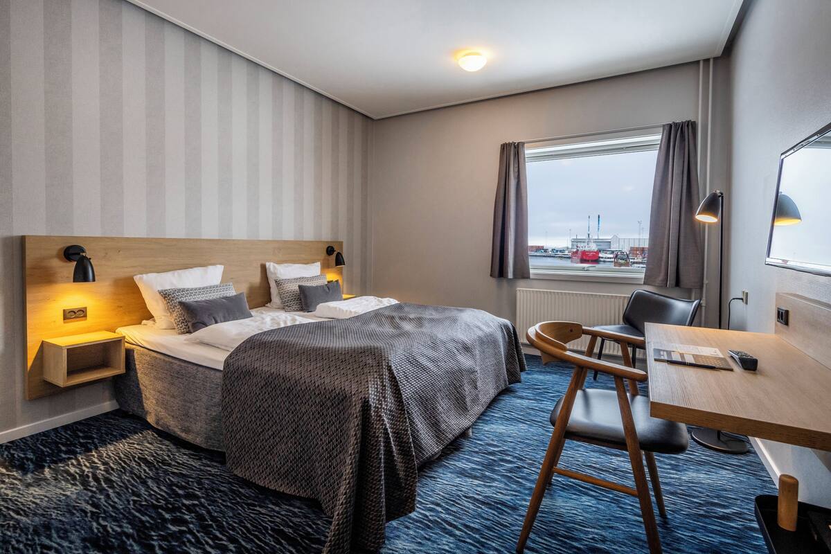 Une chambre d’hôtel avec un grand lit, des tables de chevet, un bureau avec une chaise, une fenêtre avec des rideaux et une vue sur l’extérieur.