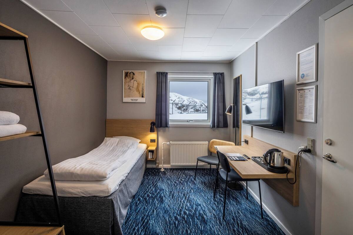Une chambre d’hôtel équipée d’un lit, d’un bureau, d’une chaise et offrant une vue sur un paysage enneigé par la fenêtre.