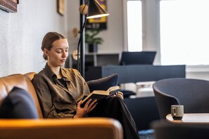 En person sitter i en modern soffa klädd i läder och läser en bok. I bakgrunden syns ett skrivbord och en stol.