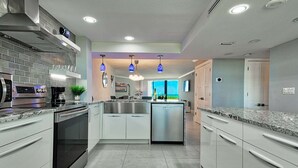 A modern kitchen with stainless steel appliances, a central island, and pendant lighting. - Updated Beachfront Getaway ~Steps to World-Class Shelling, Resort Amenities, Dining, Shops & WiFi (Marco Island)