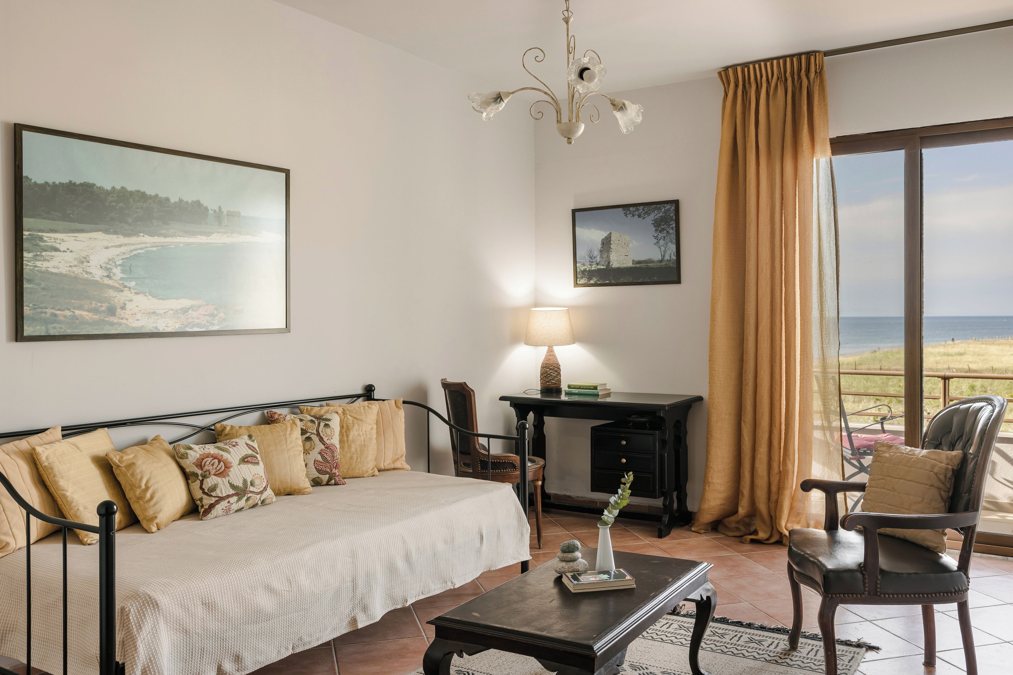 A bedroom with a bed, a desk, a chair, a lamp, and a view of the beach.