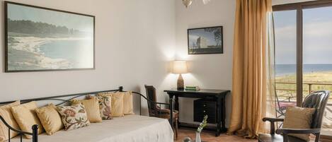 A bedroom with a bed, a desk, a chair, a lamp, and a view of the beach.