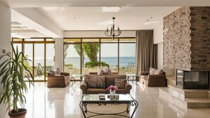 Amplia sala de estar con un gran ventanal con vistas al mar, una chimenea y una moderna lámpara de araña.