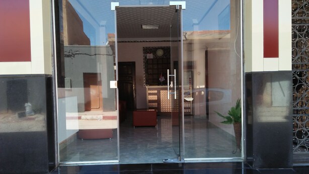 L’entrée d’un hôtel, avec une porte en verre, un comptoir d’accueil et une horloge au mur.