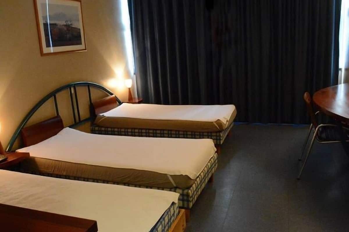 A hotel room with two single beds, a small table, and a chair.