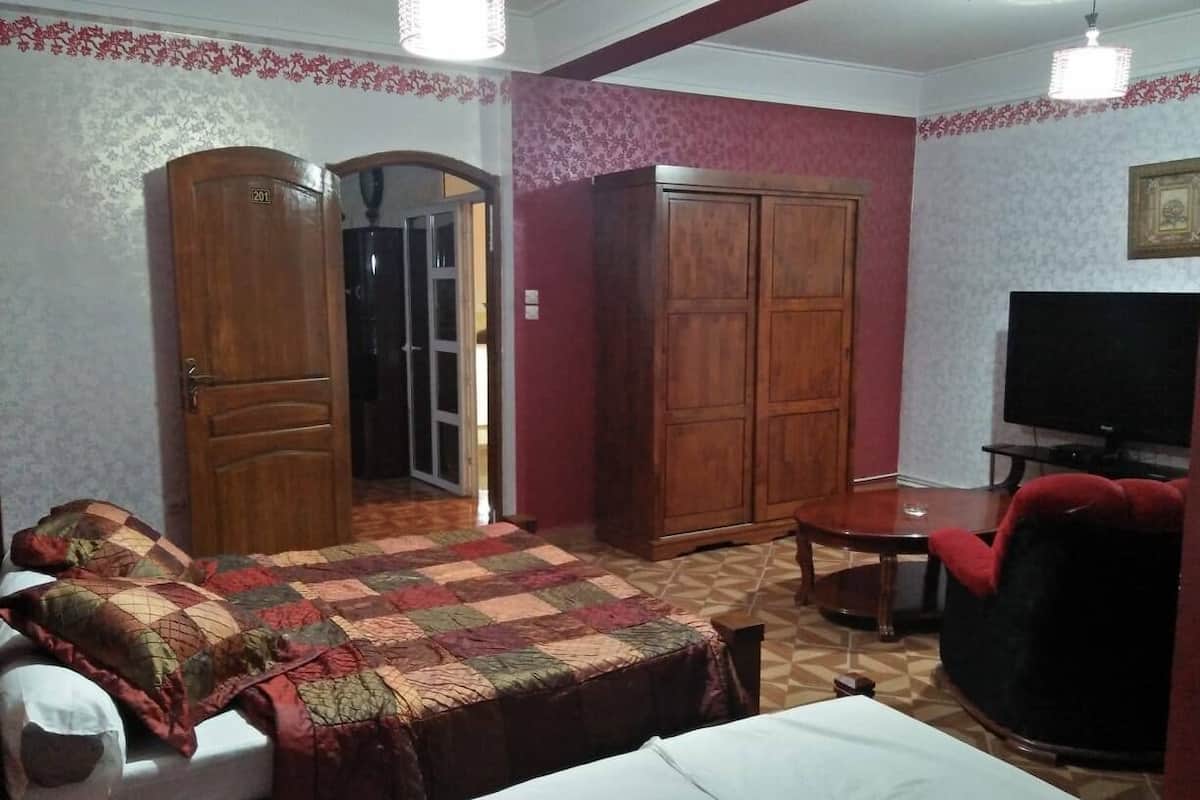 A bedroom with a bed, a TV, a wooden wardrobe, and a red chair.