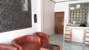 Un espace d’accueil comprenant un comptoir de réception, une porte en bois, un canapé en cuir marron et une table basse en verre.