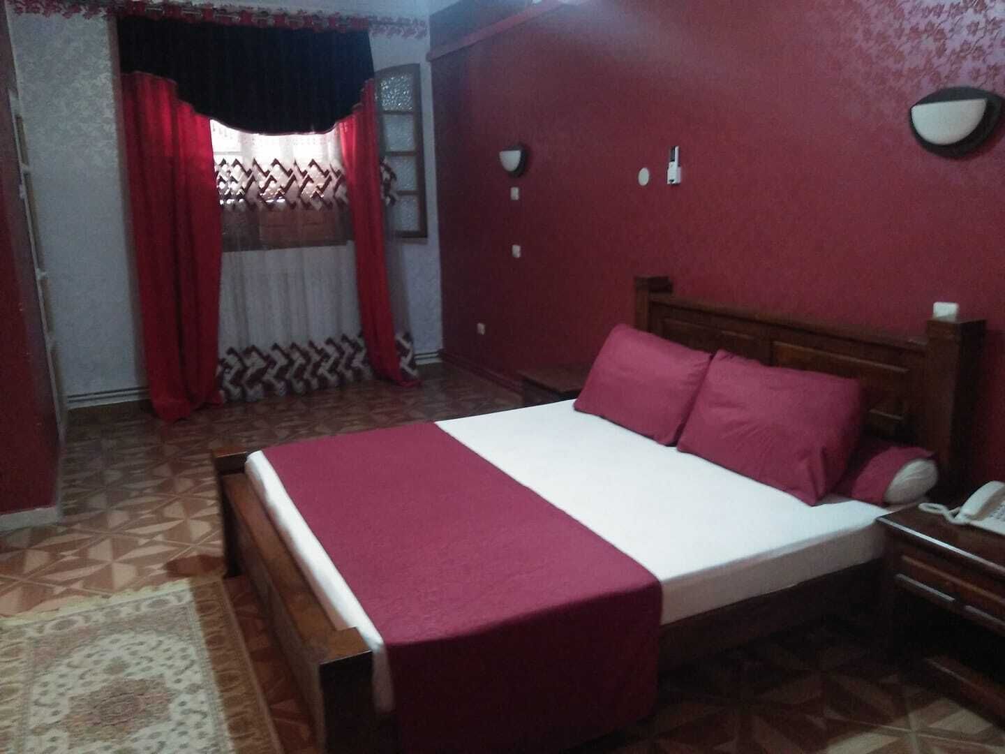 Un dormitorio con cama, mesita de noche, teléfono y ventana con cortinas.