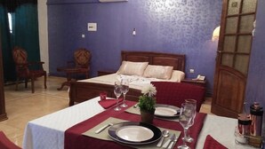 Une chambre d’hôtel avec une table à manger soigneusement dressée, un lit avec une tête de lit en bois et une petite plante en pot posée sur la table.