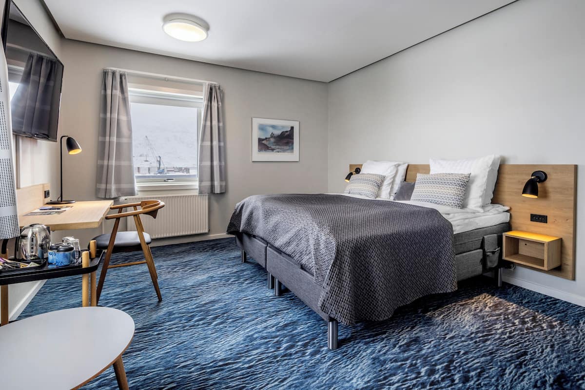 Ein modernes Hotelzimmer mit Bett, Schreibtisch, Stuhl und Blick auf die Stadtlandschaft.