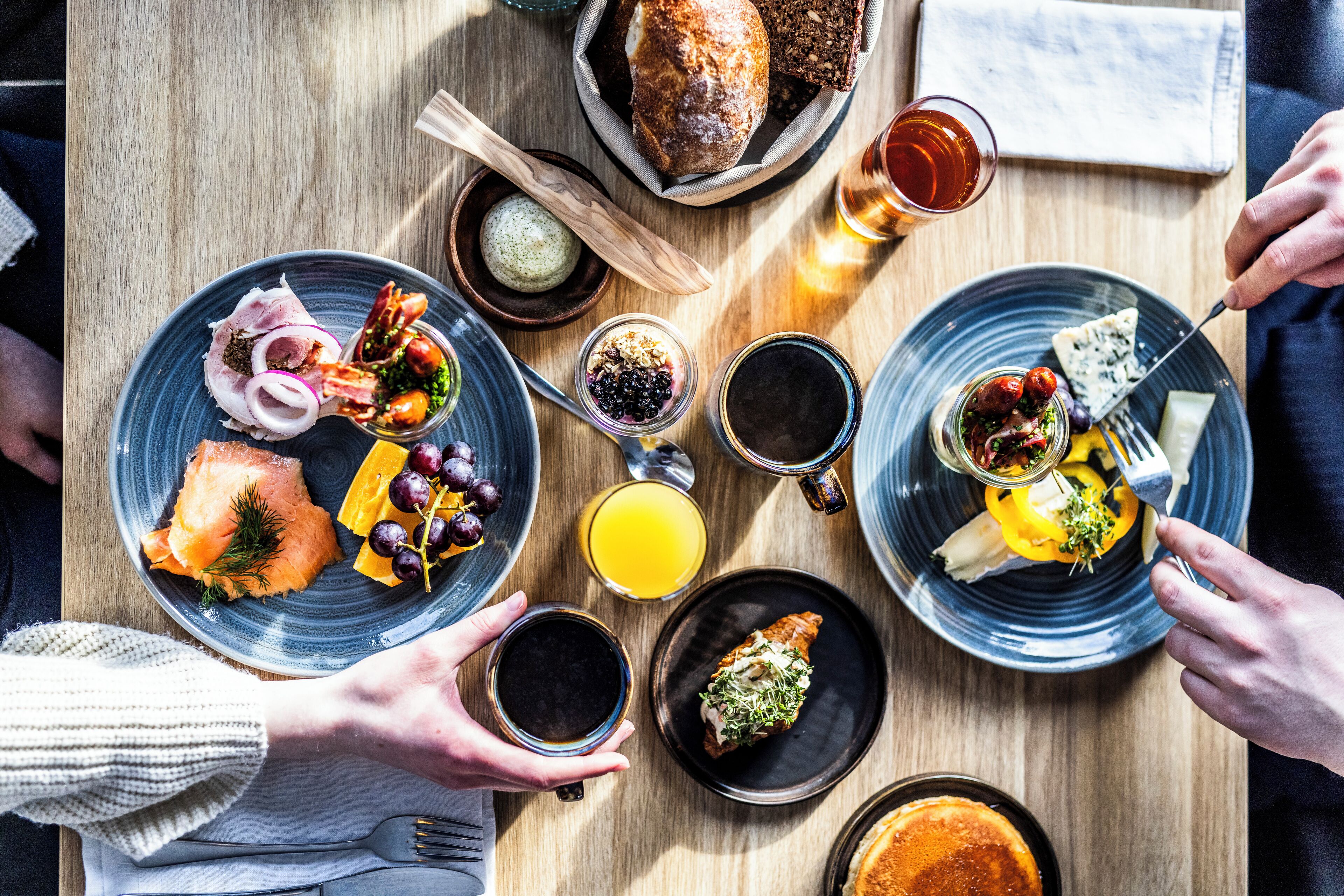 A breakfast setting with various dishes, including smoked salmon, cheese, and bread, on a wooden table.