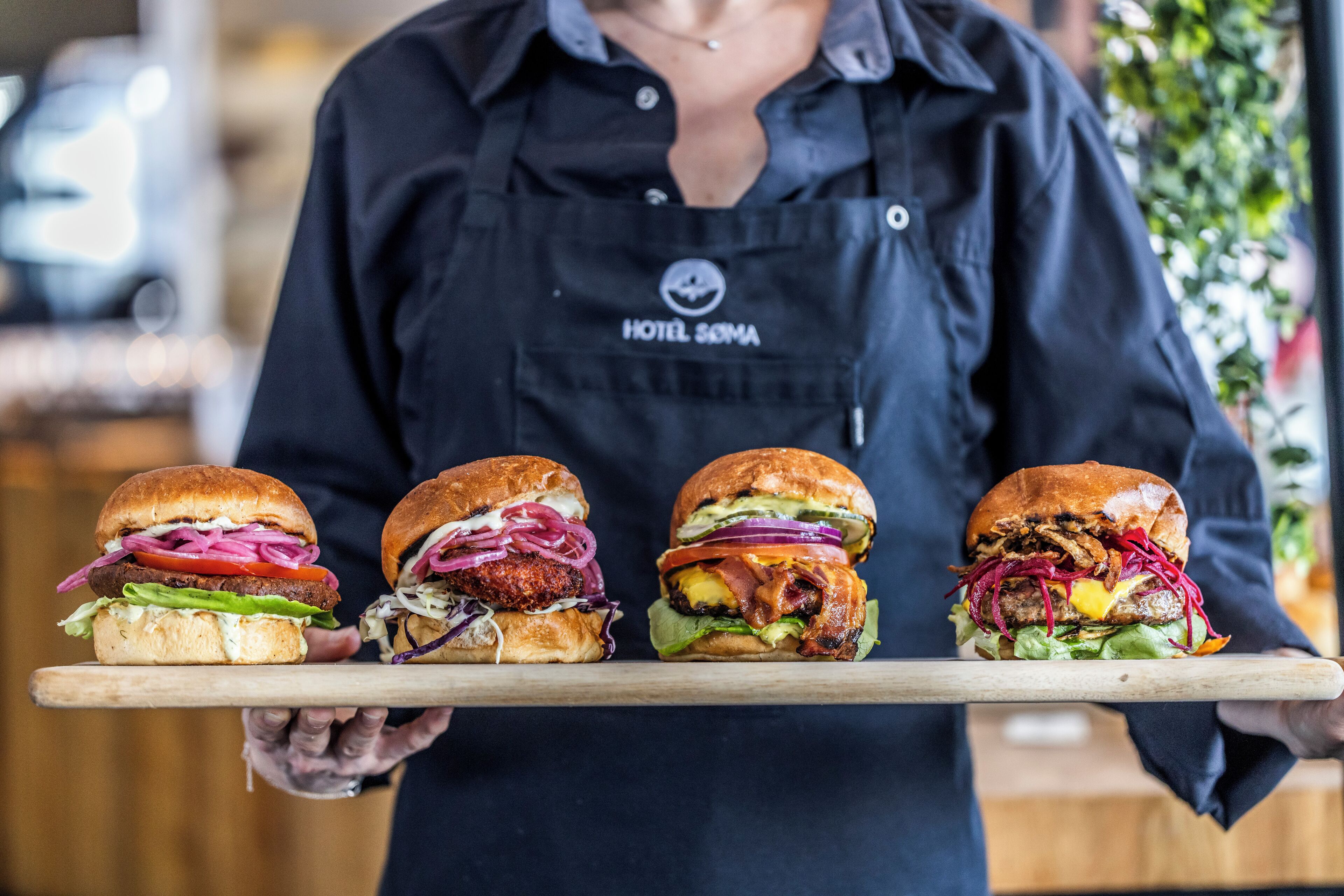 Una persona sosteniendo una tabla de madera con cuatro hamburguesas.