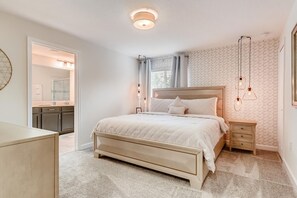 A bedroom with a bed, bedside tables, a dresser, and a bathroom visible through an open door. - 412 OC - Champions Gate (Davenport)