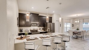 A modern kitchen with dark cabinets, stainless steel appliances, and a central island with bar stools. - 412 OC - Champions Gate (Davenport)