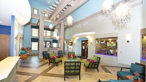 A spacious lobby with a high ceiling, a central seating area with colorful chairs, a bar area with a TV, and a large window providing natural light. - 412 OC - Champions Gate (Davenport)