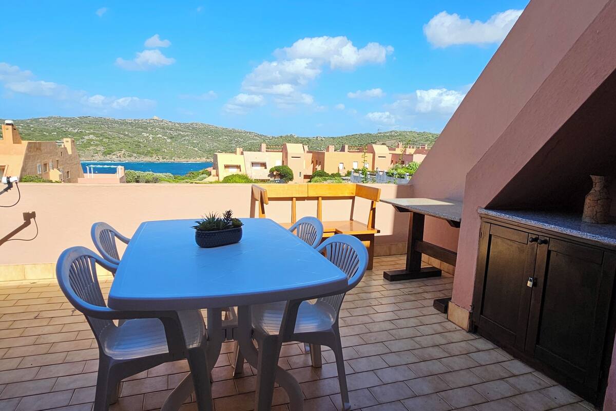 Eine Terrasse mit Tisch und Stühlen, einem Grill und Blick auf das Meer und die Hügel.