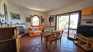 Un salon avec une cheminée, un canapé, une table à manger avec des chaises, un téléviseur et un balcon aménagé avec du mobilier d’extérieur.