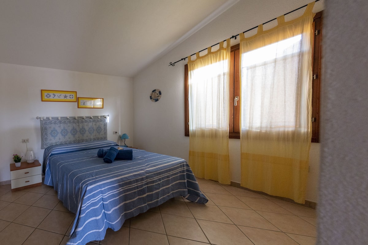 A bedroom with a bed, a nightstand, a lamp, and a window with curtains.