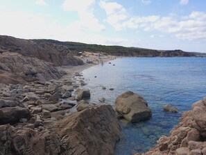 A rocky beach with clear blue water, a sandy shore, and distant hills. - Villette a Schiera Rena Majore (Aglientu)