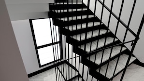Una escalera moderna con barandillas negras y peldaños de mármol, que conduce a un piso superior.