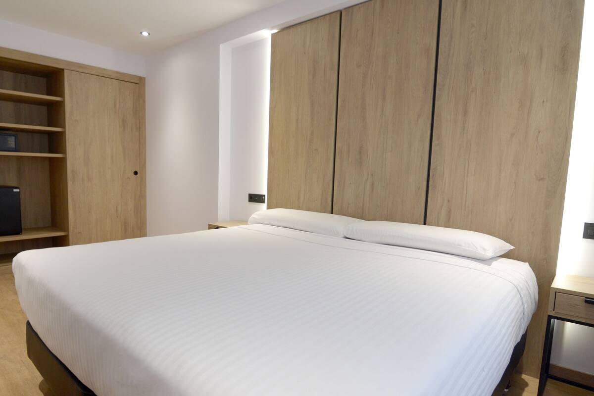 A bedroom with a large bed, wooden wardrobe, and a small desk.