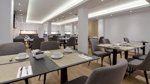 Un comedor moderno con varias mesas y sillas, equipado con vajilla básica que incluye platos, vasos y cubiertos.