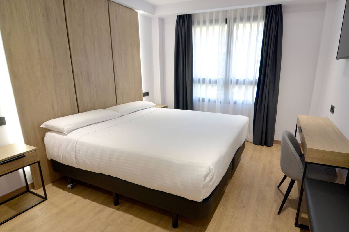 A modern hotel room with a large bed, a desk, and a TV.