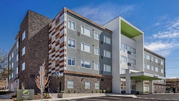 A multi-story hotel with a mix of brick and modern facade, a covered parking area, and a sign indicating the name and location.