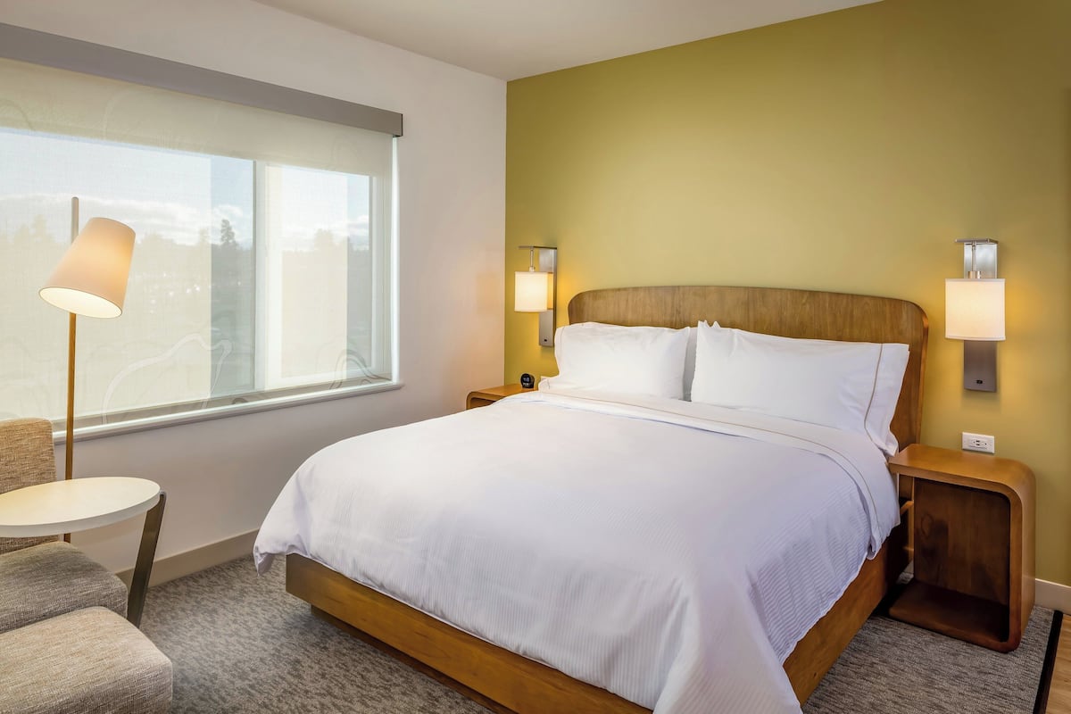 A hotel room with a large bed, two bedside lamps, a small table, and a chair.