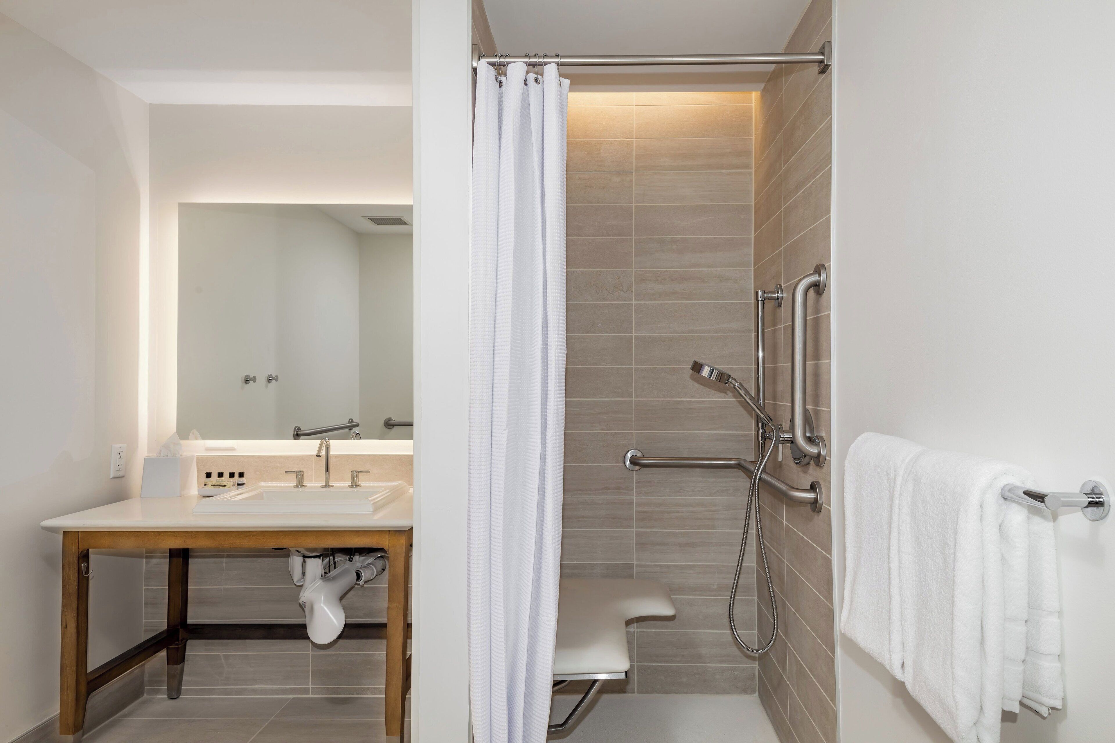Un baño moderno con ducha, barras de apoyo, lavamanos y toallero.