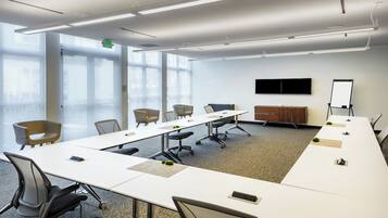 A conference room with a long table, chairs, a whiteboard, and a TV on the wall.