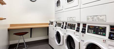 A laundry room with multiple washing machines, a clock, and a wooden counter.