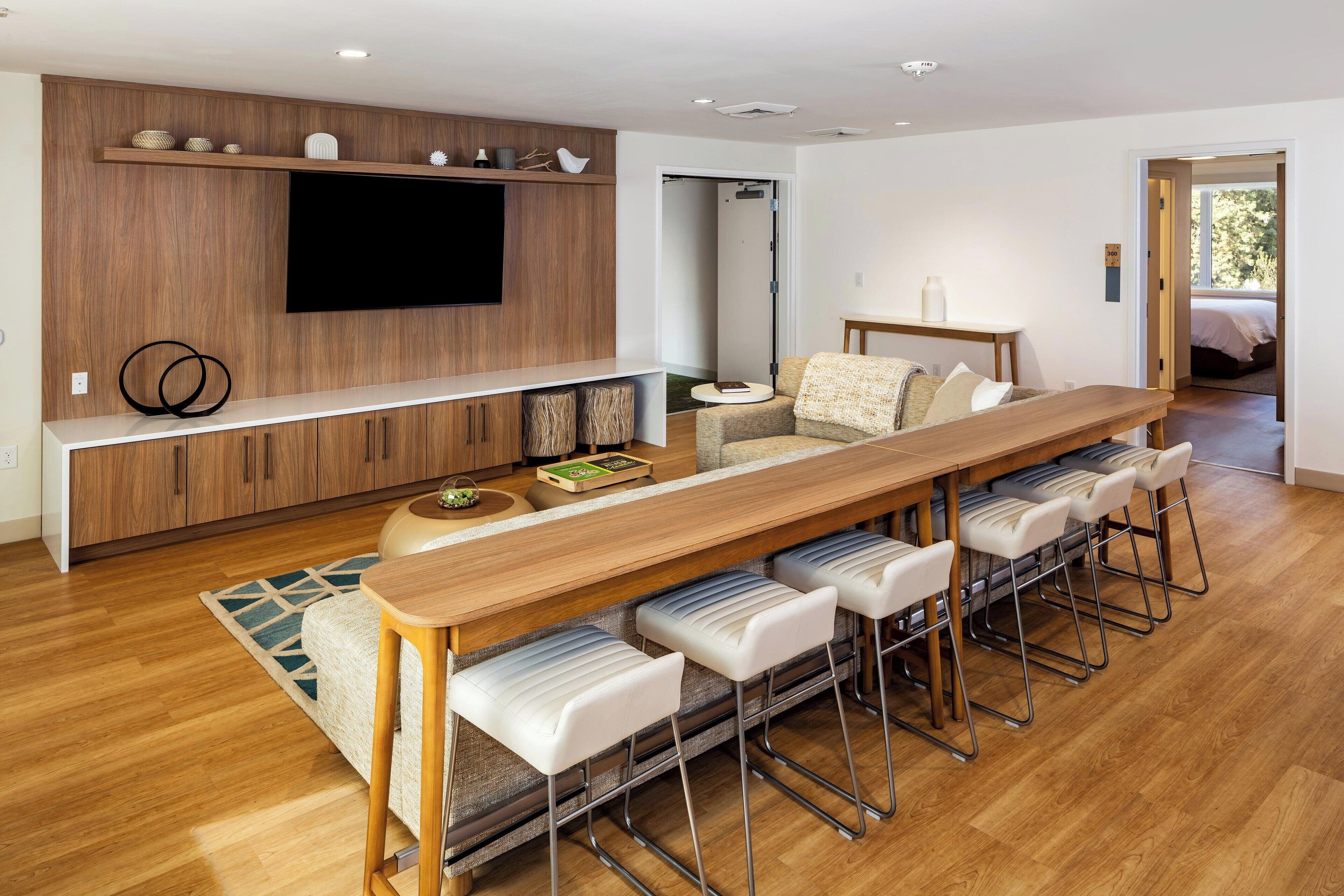 A modern kitchen with a wooden countertop, bar stools, and a flat-screen TV mounted on the wall.