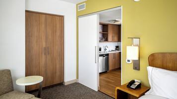 Une chambre d’hôtel comprenant un lit, une petite table, une armoire, un coin cuisine et une lampe de chevet.
