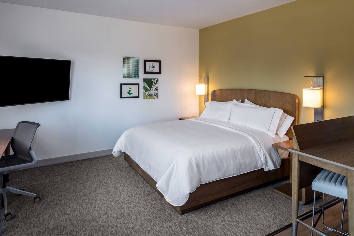 A hotel room with a bed, a desk, a chair, a flat-screen TV, and wall-mounted artwork.