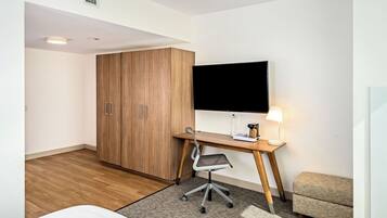 Een hotelkamer met een houten garderobe, een bureau met stoel, een flatscreen televisie, een nachtkastje met lamp en een kleine zithoek.