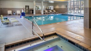 En indendørs swimmingpool med solbeskinnelig område, liggestole og siddepladser ved poolen.