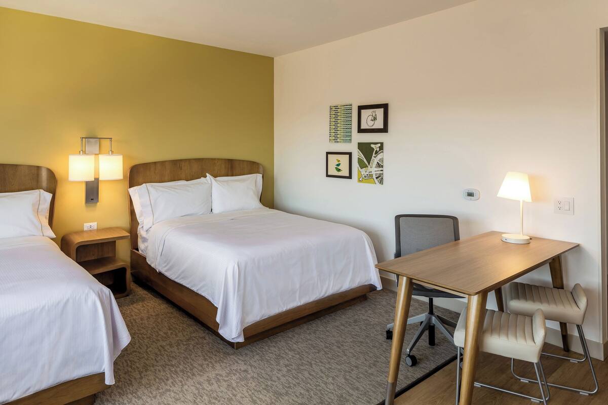 A hotel room with two single beds, a wooden desk with a chair, a small table, and a lamp.
