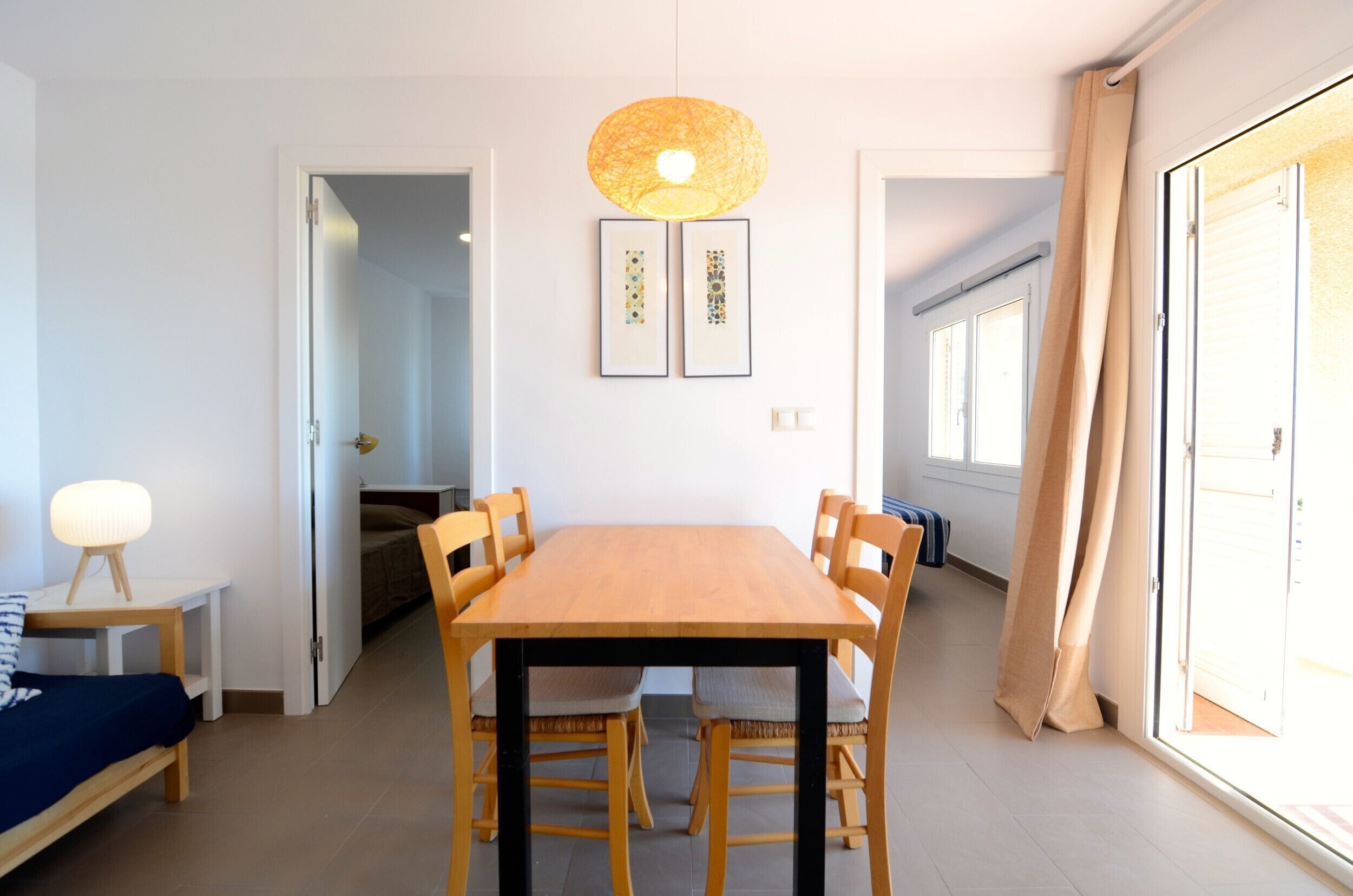 A dining area with a wooden table and chairs, a hanging light fixture, and two framed artworks on the wall.