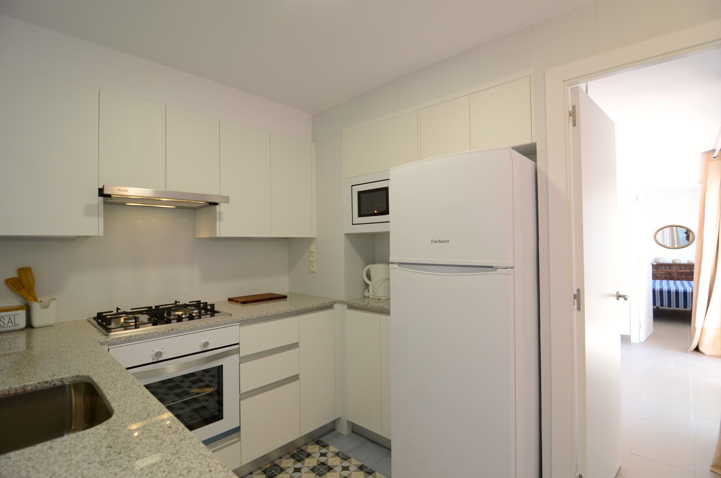 Una cocina compacta con armarios blancos, cocina a gas, microondas y refrigerador.