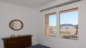 Une chambre à coucher comprenant un lit, une commode, un miroir et une fenêtre donnant sur une plage et des collines.