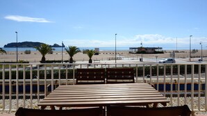 Une table et des bancs en bois offrent une vue sur une plage bordée de palmiers, une île lointaine et un ciel dégagé.