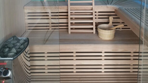 A sauna with wooden benches, a stone wall, and a ceiling with blue lighting. - Sula Rorbuer og Havhotell (Frøya)