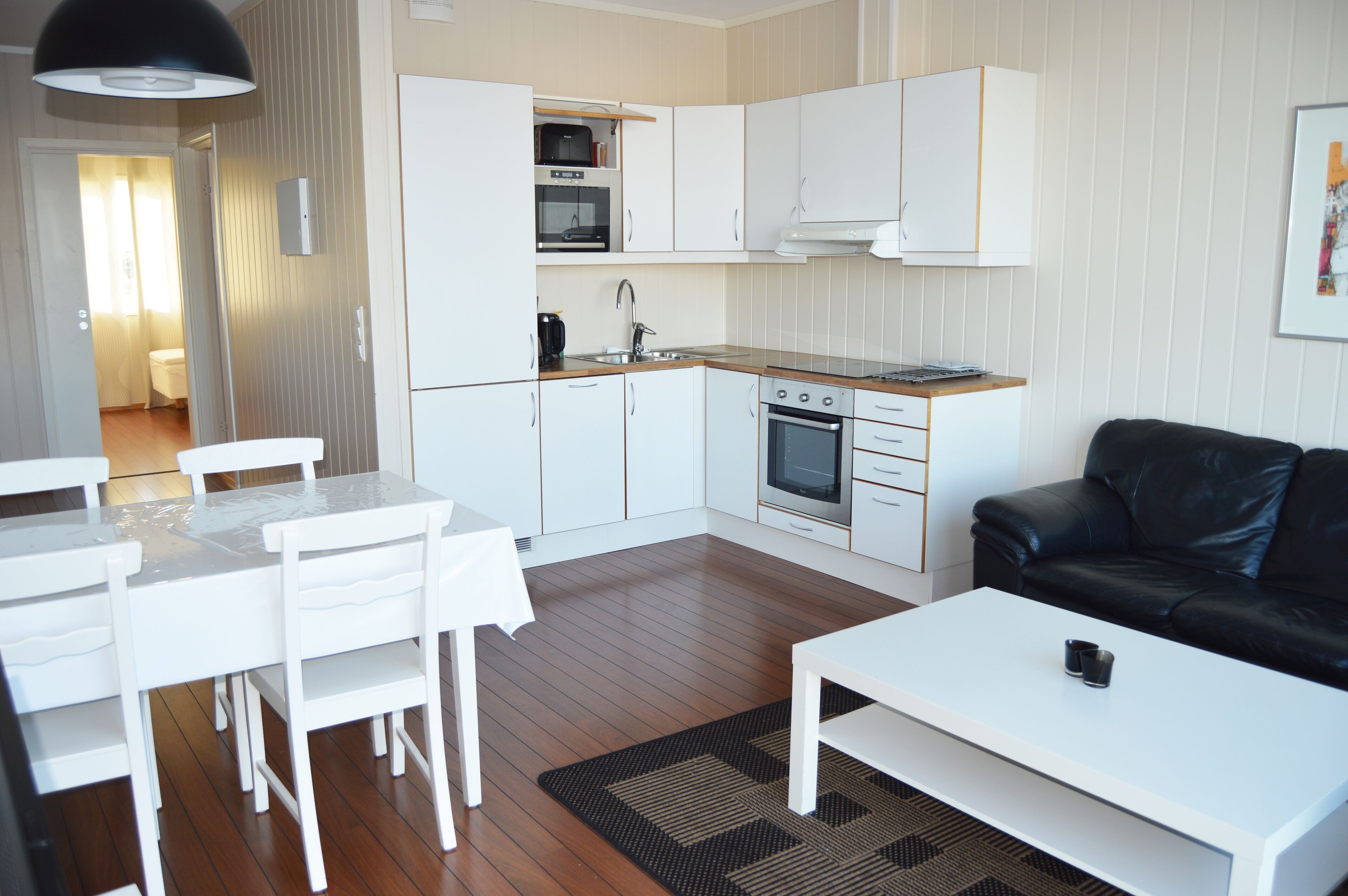 Una cocina moderna con gabinetes blancos, una mesa de comedor con sillas, un sofá de cuero negro y una mesa de centro blanca.