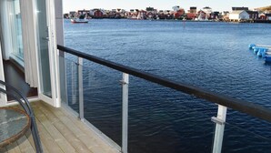 A view from a balcony with a railing overlooking a body of water, a dock with boats, and a row of red buildings in the background. - Sula Rorbuer og Havhotell (Frøya)