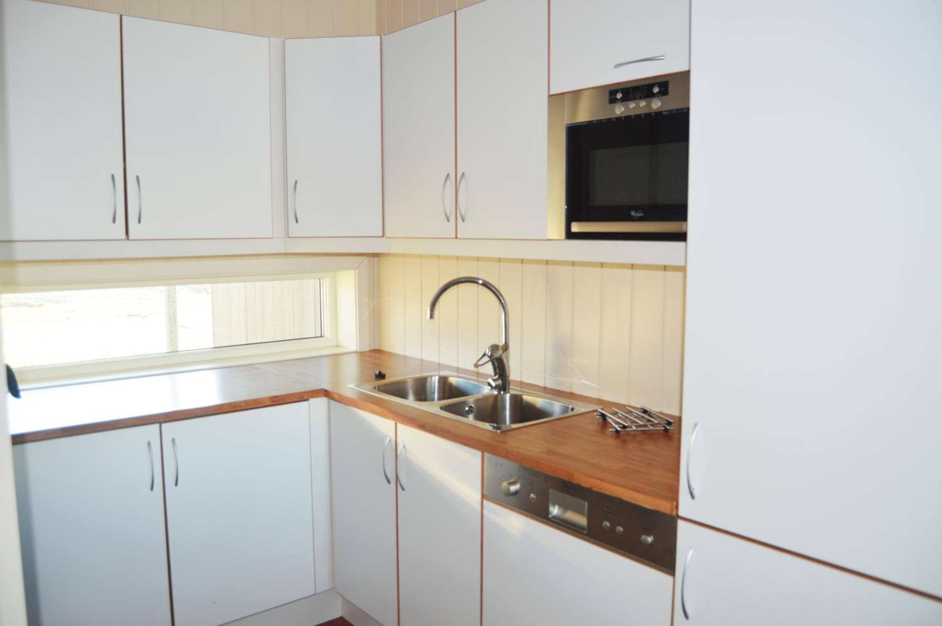 Una cocina con armarios blancos, un lavamanos de acero inoxidable, horno empotrado y encimera de madera.